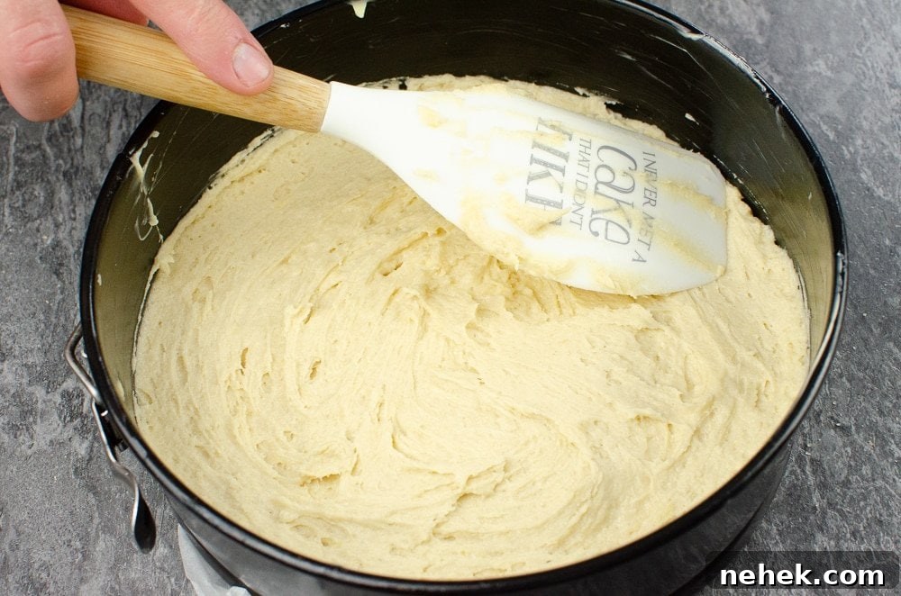 Perfect Lemon Drizzle Cake Recipe — Moist, Zesty Slice 19 Cake mixture being spread into a black round cake tin with a wooden and white spatula