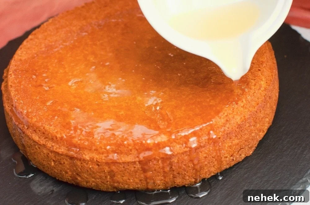 Perfect Lemon Drizzle Cake Recipe — Moist, Zesty Slice 23 Pouring lemon syrup from a white pot over the lemon cake on black slate