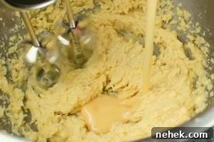 Perfect Lemon Drizzle Cake Recipe — Moist, Zesty Slice 7 Egg being poured into the cake mixture in a silver bowl and being whisked with a silver whisk