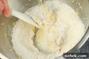 Perfect Lemon Drizzle Cake Recipe — Moist, Zesty Slice 8 Flour being added to the butter mixture in a silver bowl and being folded with a white and wooden spatula