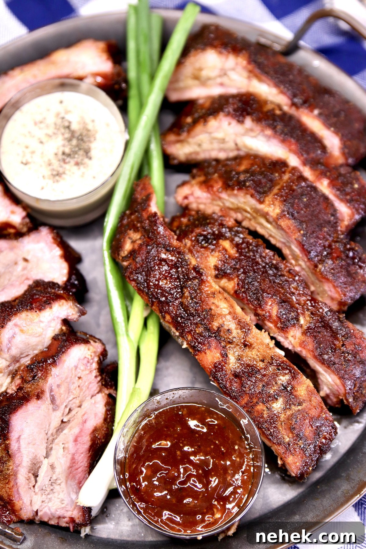 How to Grill the most tender baby back ribs. Closeup of platter of sliced baby back ribs, green onions, bowls of sauce.
