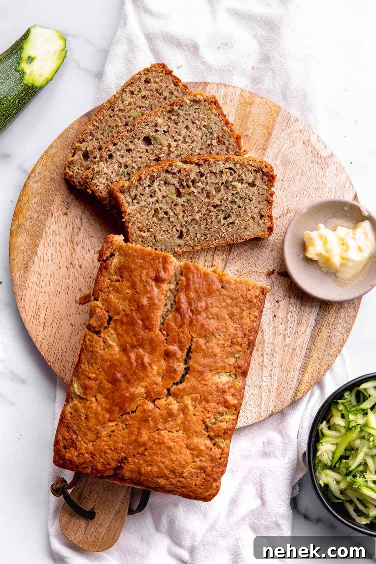 Moist Sourdough Zucchini Bread Recipe 2 A loaf of zucchini bread sitting on a wooden board with shredded zucchini.