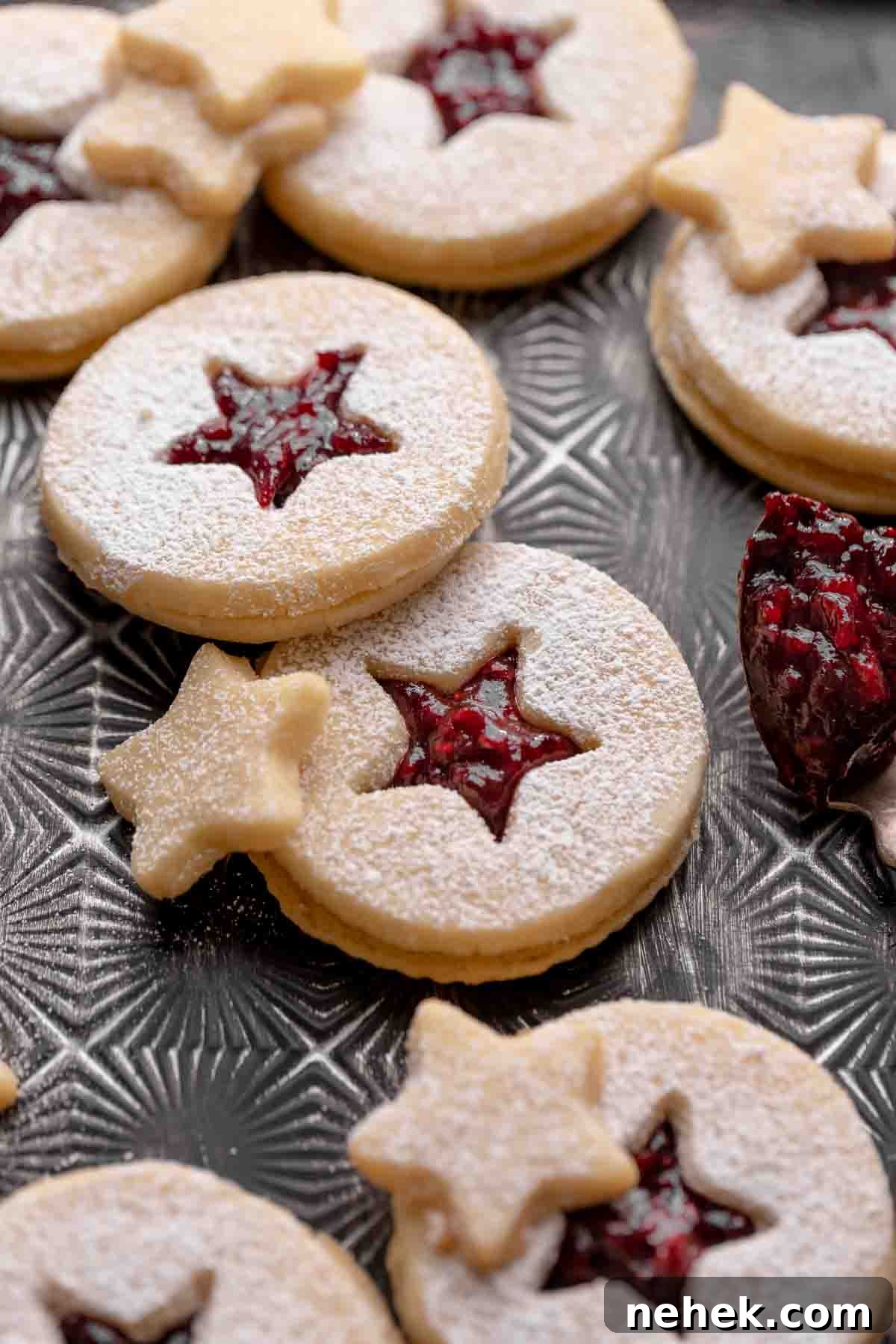 Raspberry Jam Linzer Shortbread Cookies 2 raspberry linzer cookies filled with jam and dusted with powdered sugar on a black tray.