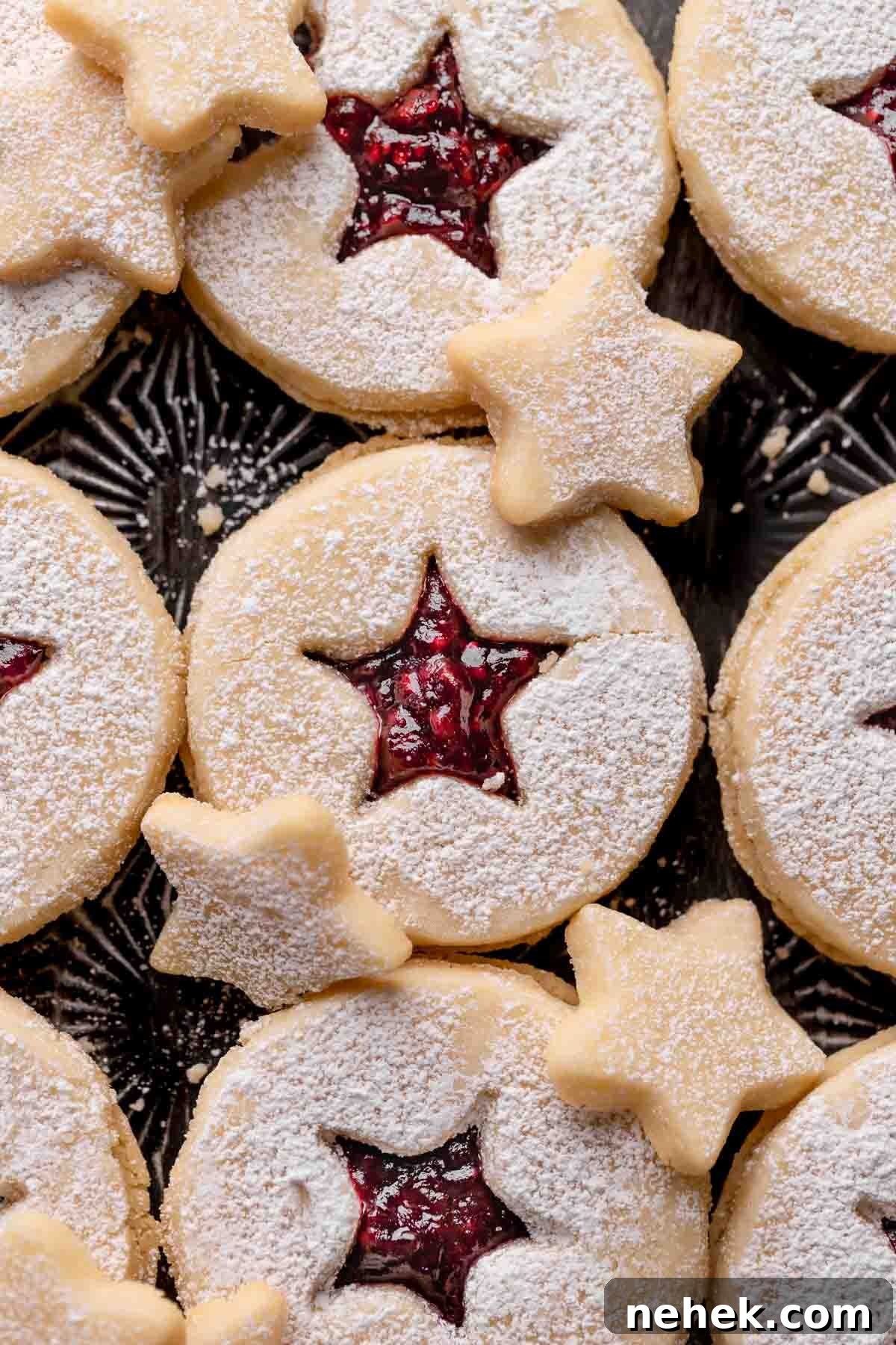 Raspberry Jam Linzer Shortbread Cookies 3 linzer tart cookies with raspberry jam on a black baking tray.