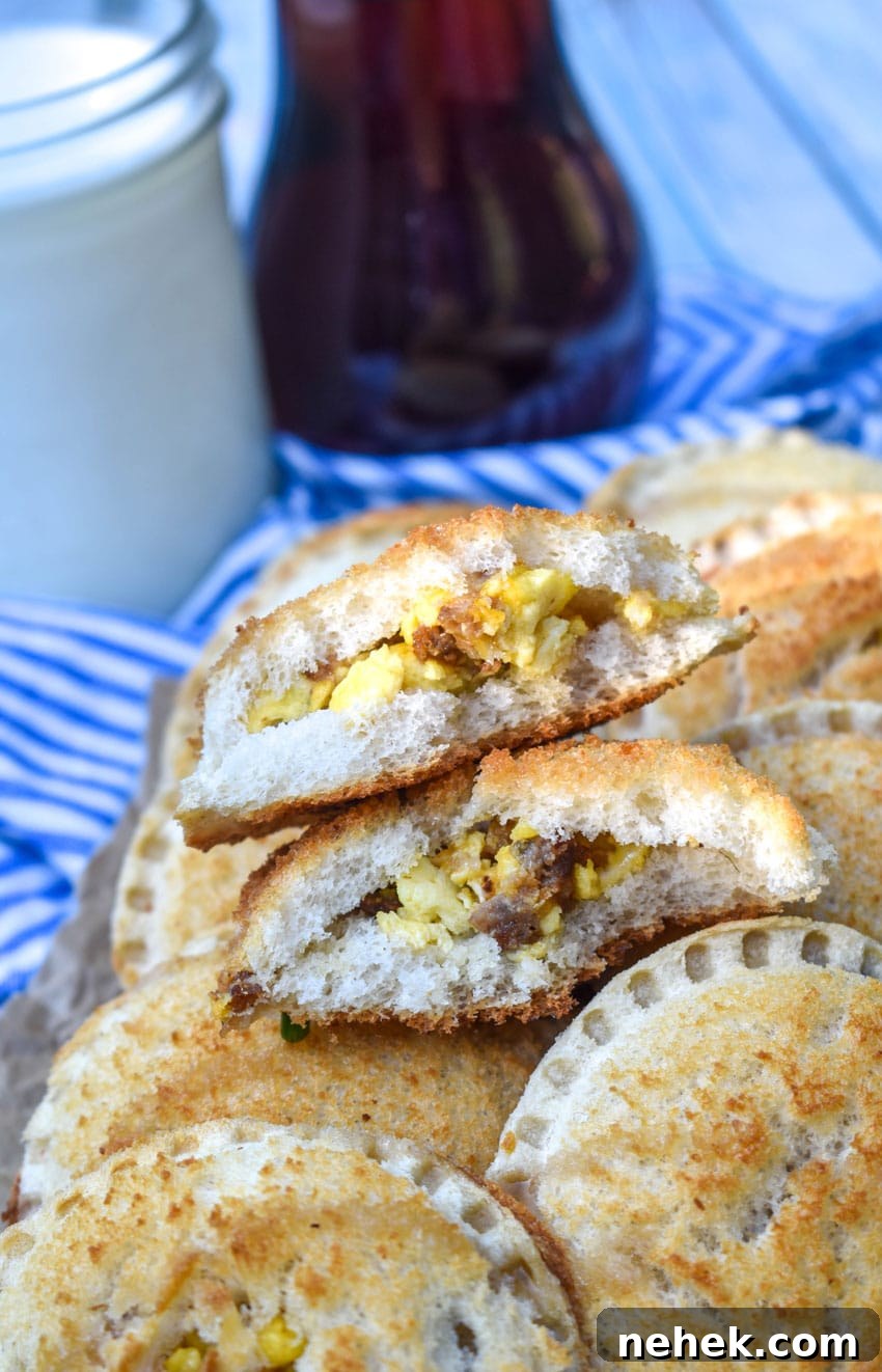 Breakfast Uncrustables: Make-Ahead Morning Sandwiches 6 a broken in half breakfast uncrustable revealing the sausage egg and cheese filling is sitting on a pile of uncurstables