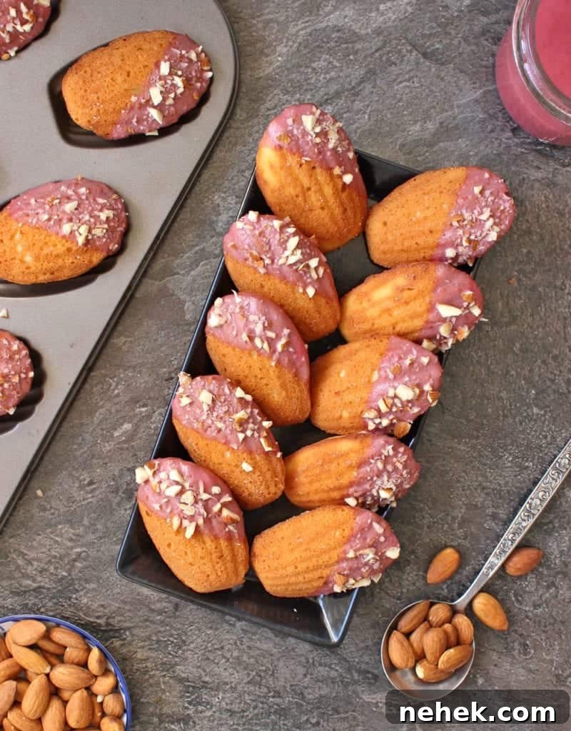 Almond Madeleines with Raspberry Glaze Recipe 3 Cakes placed on a black rectangular plate next to the madeleine pan