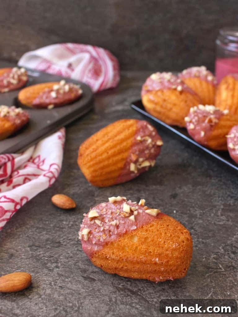 Almond Madeleines with Raspberry Glaze Recipe 4 One madeleine on its side on a grey surface with almonds.