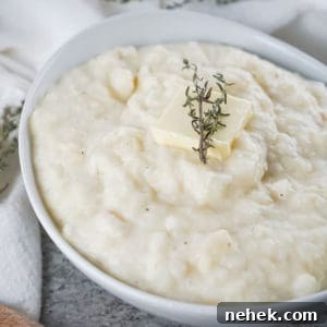 Creamy Mashed Potatoes and Parsnips Recipe 7 Close up shot of potato and parsnip mash with a pad of butter and herbs in a white bowl on a white cloth.