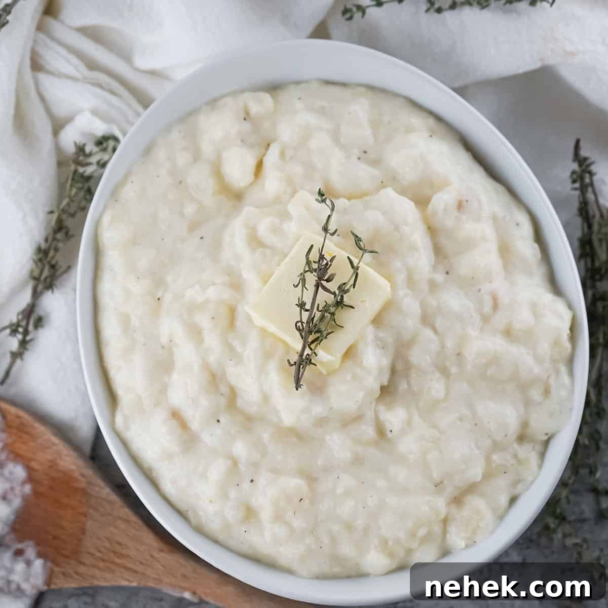 Creamy Mashed Potatoes and Parsnips Recipe 5 Overhead shot of parsnip and potato mash with a pad of butter and herbs in a white bowl with a wooden spoon on the side.