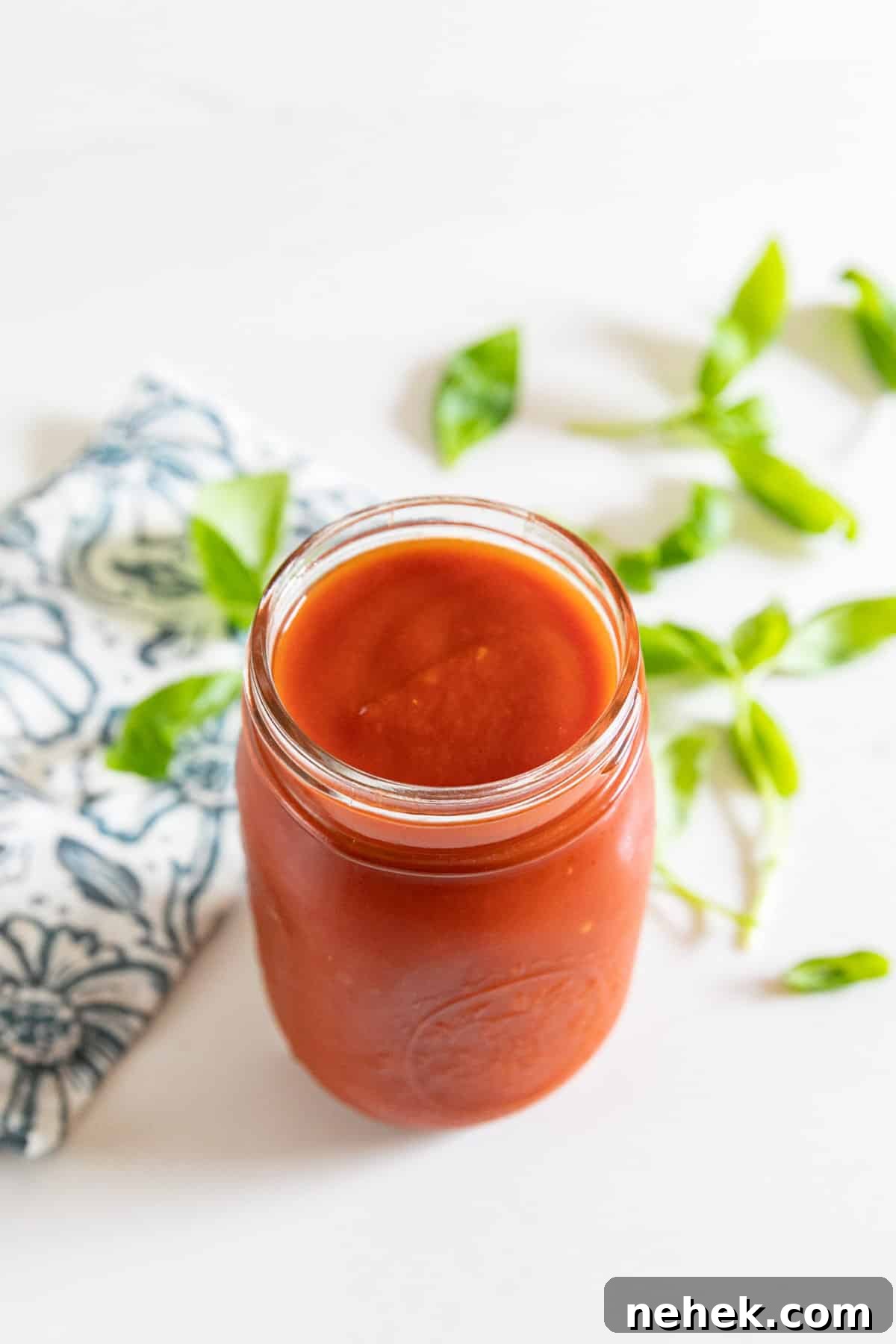 Homemade Sugar-Free Marinara Sauce 9 A jar of marinara sauce from above with a napkin and basil behind it.
