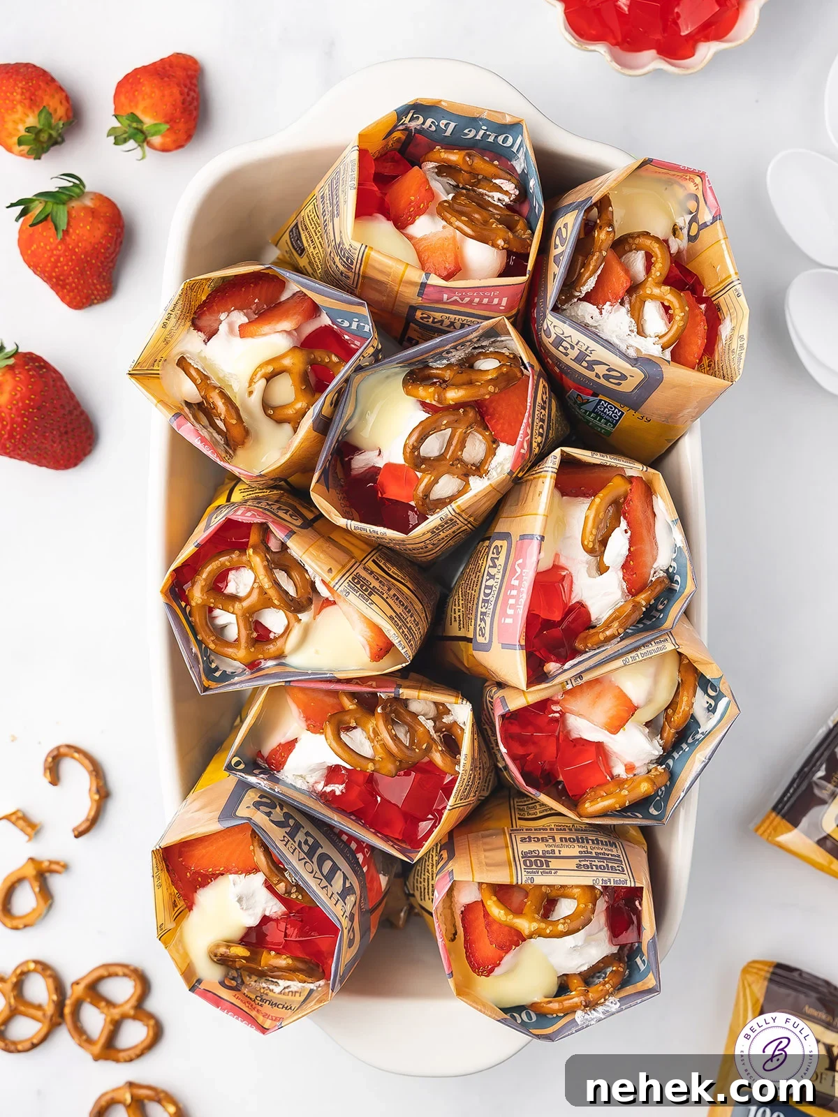 Made with cheesecake pudding, strawberry jello, whipped cream, and pretzels, this Walking Strawberry Pretzel Salad is a fun, portable dessert. Overhead view of bags of walking strawberry pretzel salad standing up in a baking dish